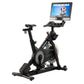 Black indoor stationary exercise bike with touchscreen display console mounted on adjustable arm, shown on white background
