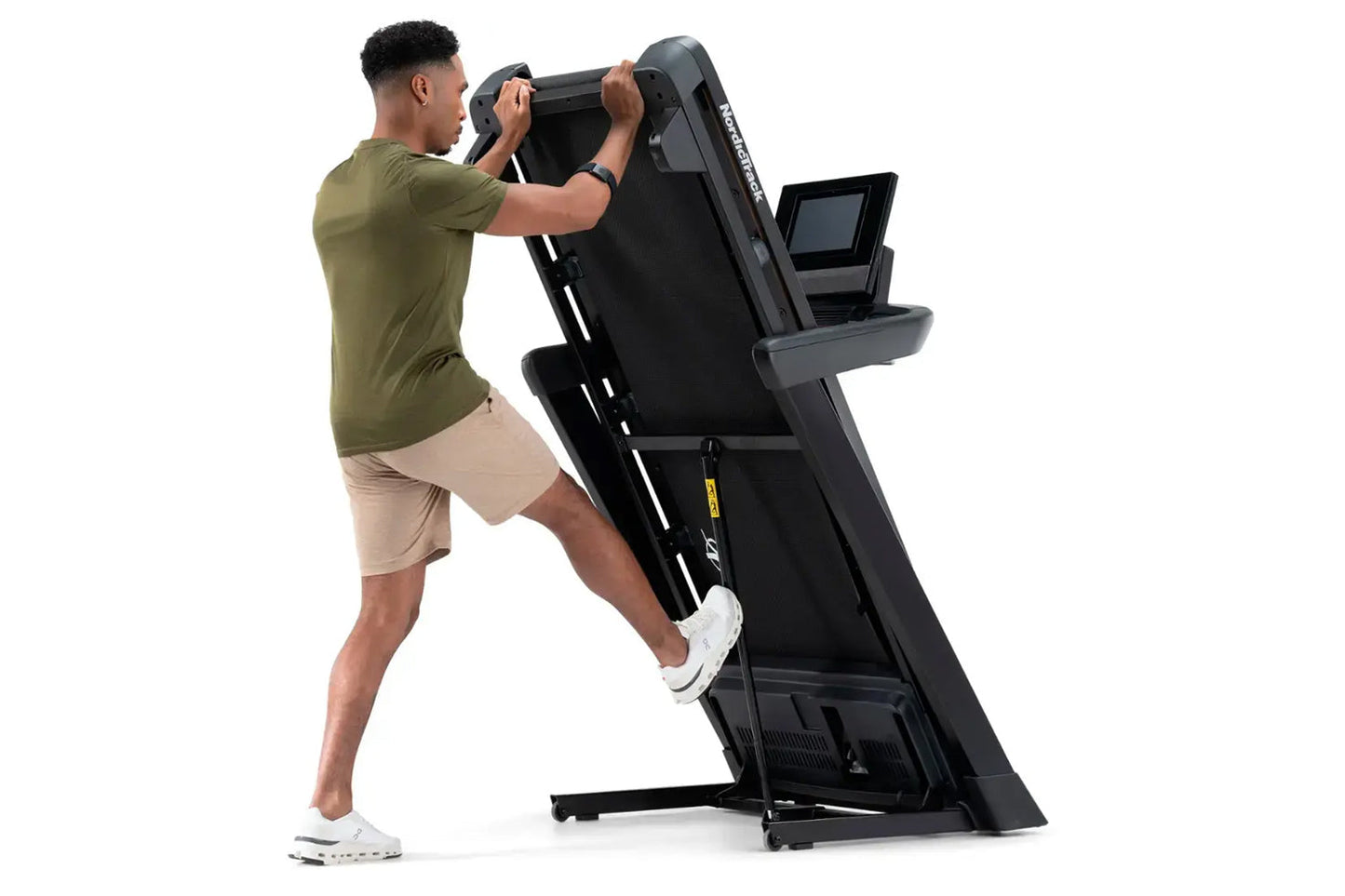Man using black NordicTrack T-Series 10 treadmill with digital display, wearing olive green shirt and beige shorts