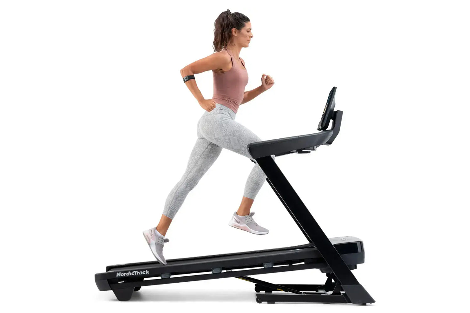 Woman running on NordicTrack black treadmill wearing mauve tank top and gray leggings, white sneakers, on white background