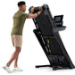 Man in olive t-shirt and tan shorts using black NordicTrack T-Series treadmill with digital display on white background