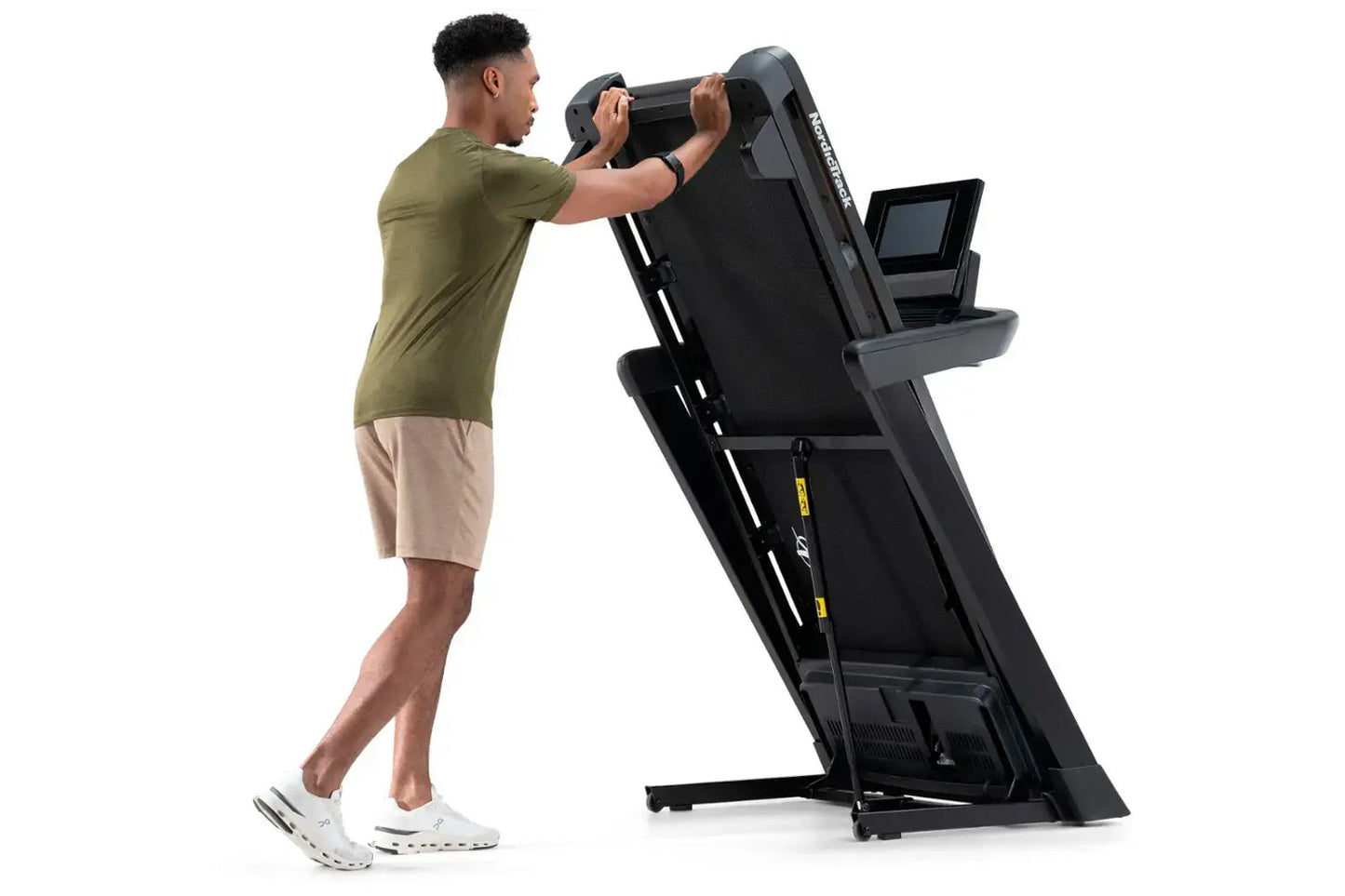 Man in olive t-shirt and tan shorts using black NordicTrack T-Series treadmill with digital display on white background