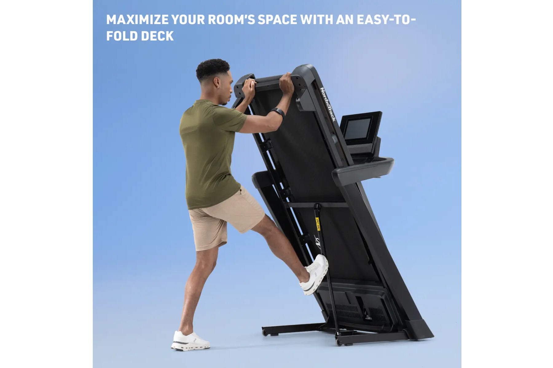 Man in olive shirt and beige shorts using black NordicTrack treadmill with digital display, folded upright position on blue b