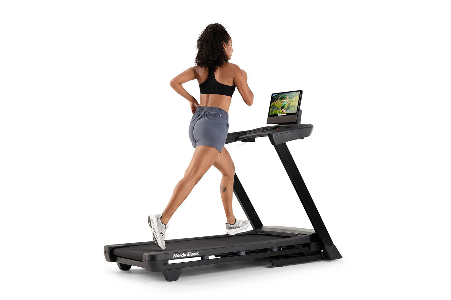 Black NordicTrack treadmill with tablet holder, worn by model in black sports bra and gray shorts, on white background
