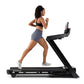 Woman running on NordicTrack black treadmill wearing black sports bra and gray shorts, white sneakers, on white background
