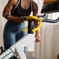 Woman in black sports bra and blue leggings riding stationary bike with yellow handlebar tape, white and teal frame