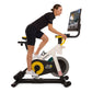 Woman in black athletic wear riding NordicTrack stationary bike with yellow wheel and display screen, white background