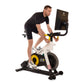Man wearing black shirt and shorts riding Tour de France stationary bike with yellow flywheel and digital monitor display