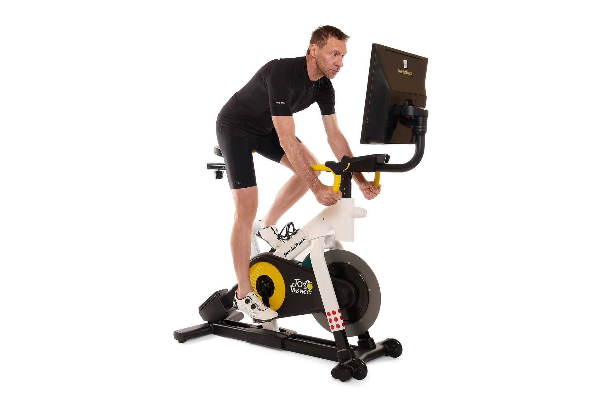 Man wearing black shirt and shorts riding Tour de France stationary bike with yellow flywheel and digital monitor display