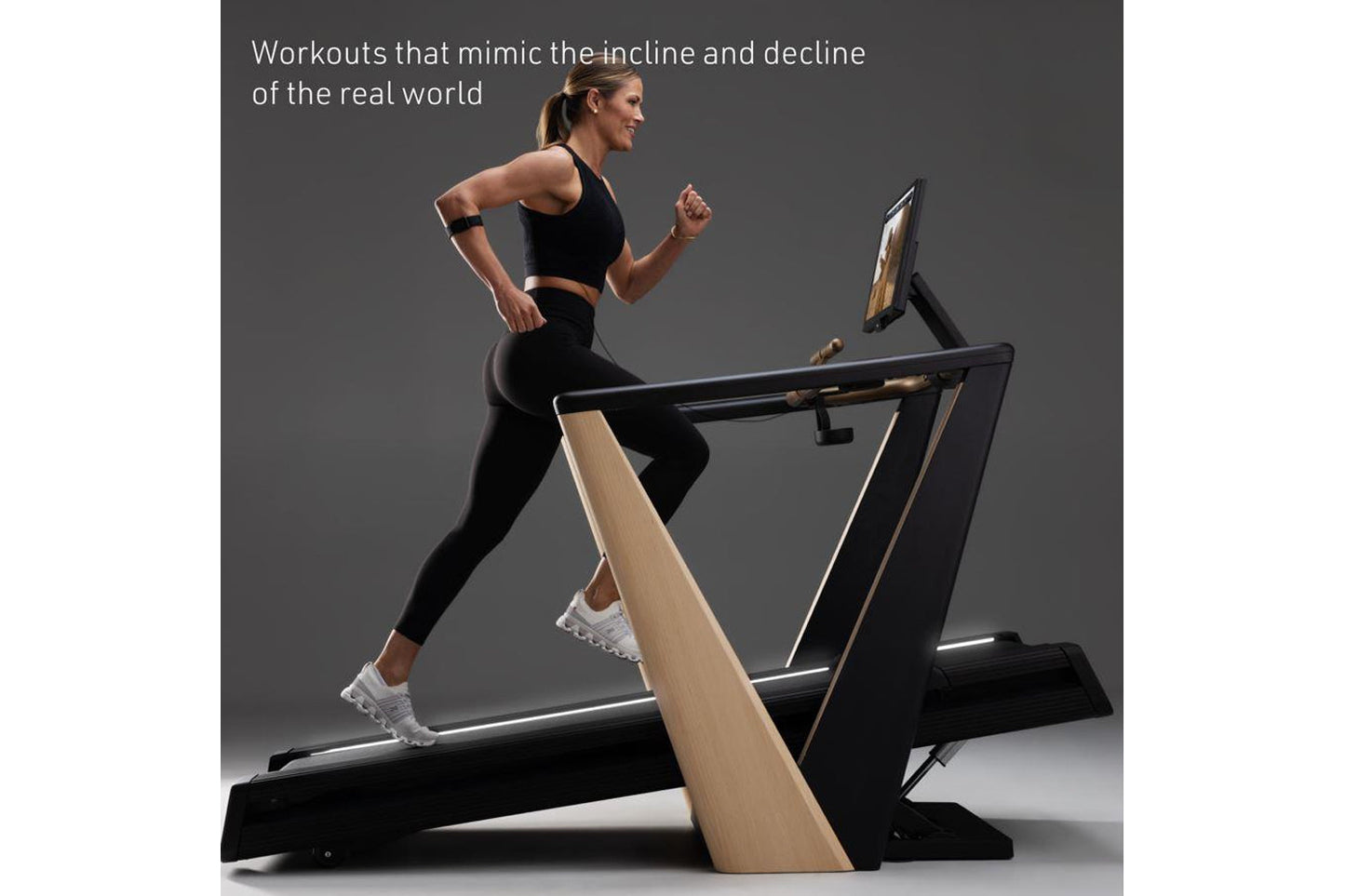 Woman running on black and natural wood incline treadmill with digital display, wearing black sports bra and leggings with wh