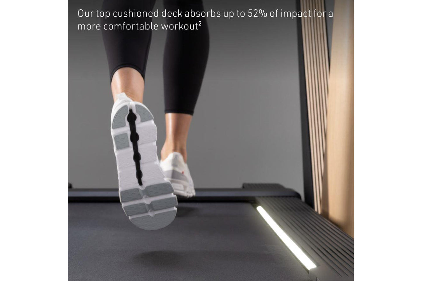 Person in black leggings and white running shoes on cushioned treadmill deck, shown from below during workout