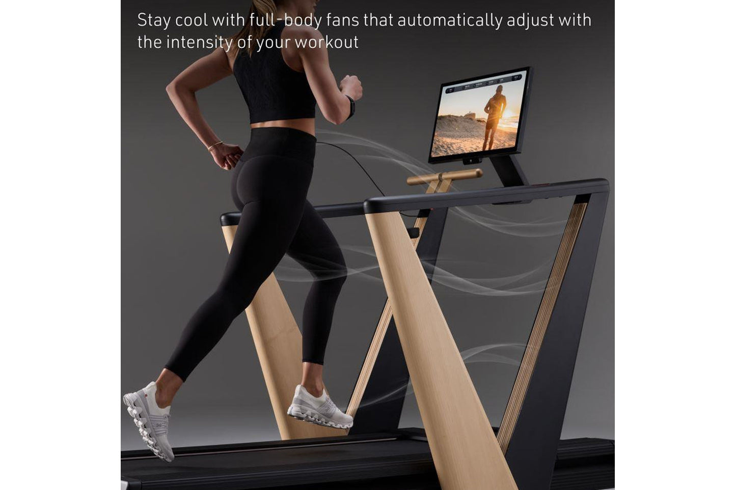 Woman running on treadmill with black deck and natural wood frame, tablet display mounted showing outdoor scene, air flow vis