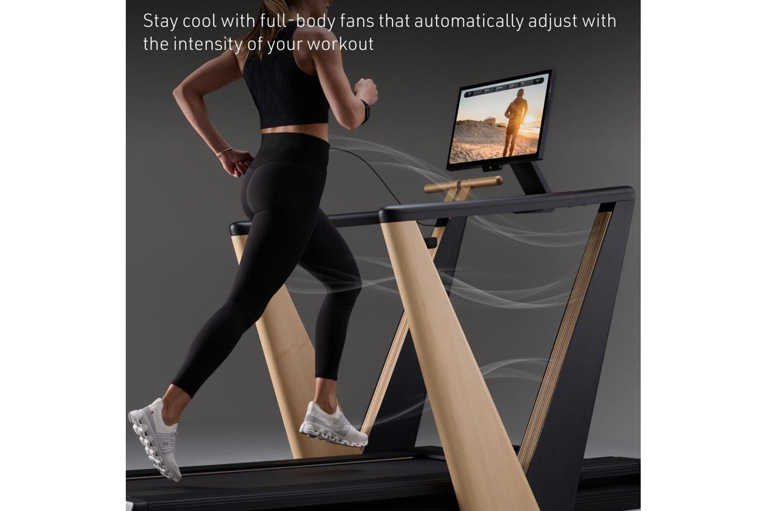 Woman running on treadmill with black deck and natural wood frame, tablet display mounted showing outdoor scene, air flow vis