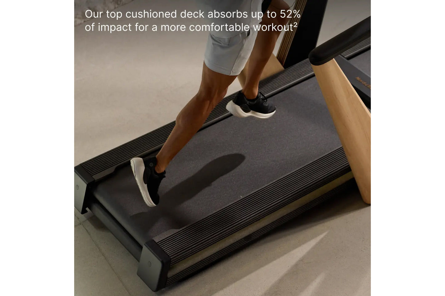 Person jogging on black treadmill with cushioned deck, wearing black and white sneakers and light blue shorts