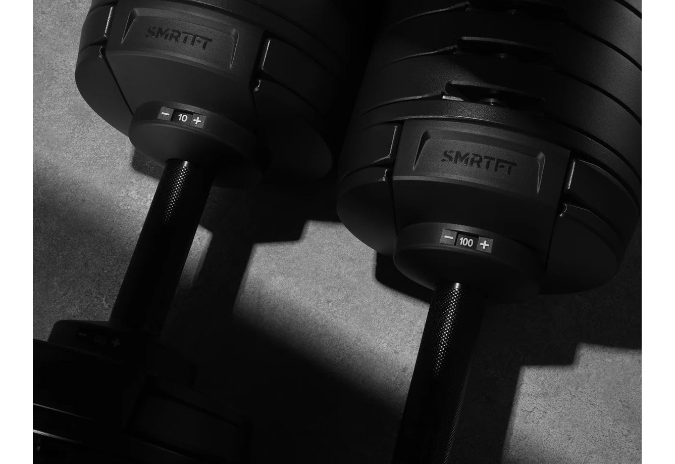 Pair of black NÜOBELL adjustable dumbbells marked 10 lb and 100 lb with textured grips, displayed on gray background