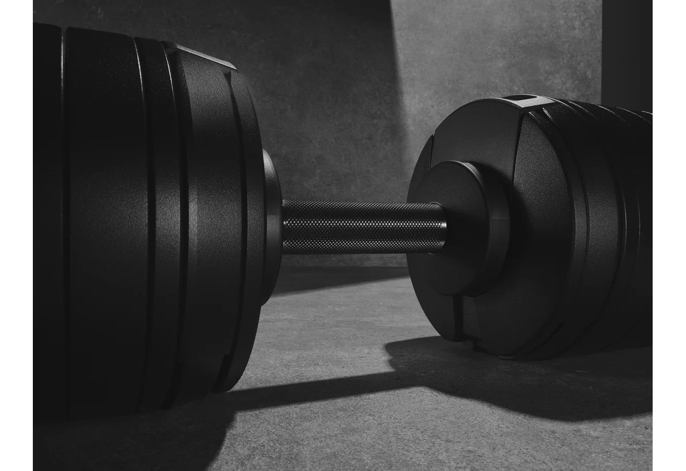 Black adjustable dumbbells with textured knurled handles and weight plates, displayed on concrete floor in black and white ph