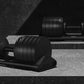 Matte black adjustable dumbbells with ribbed weight plates on stand, displayed on concrete floor