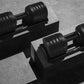 Pair of black adjustable dumbbells with ribbed plates on dark stands, flat lay view