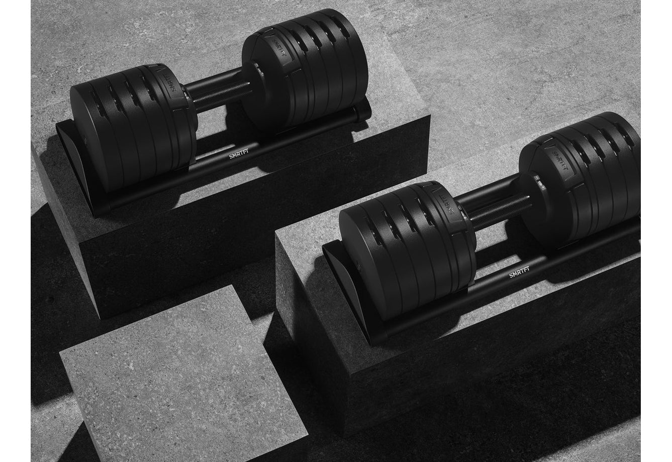 Pair of black adjustable dumbbells with ribbed plates on dark stands, flat lay view