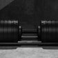 Pair of black adjustable dumbbells with ribbed weight plates on matching base, viewed from above on concrete floor