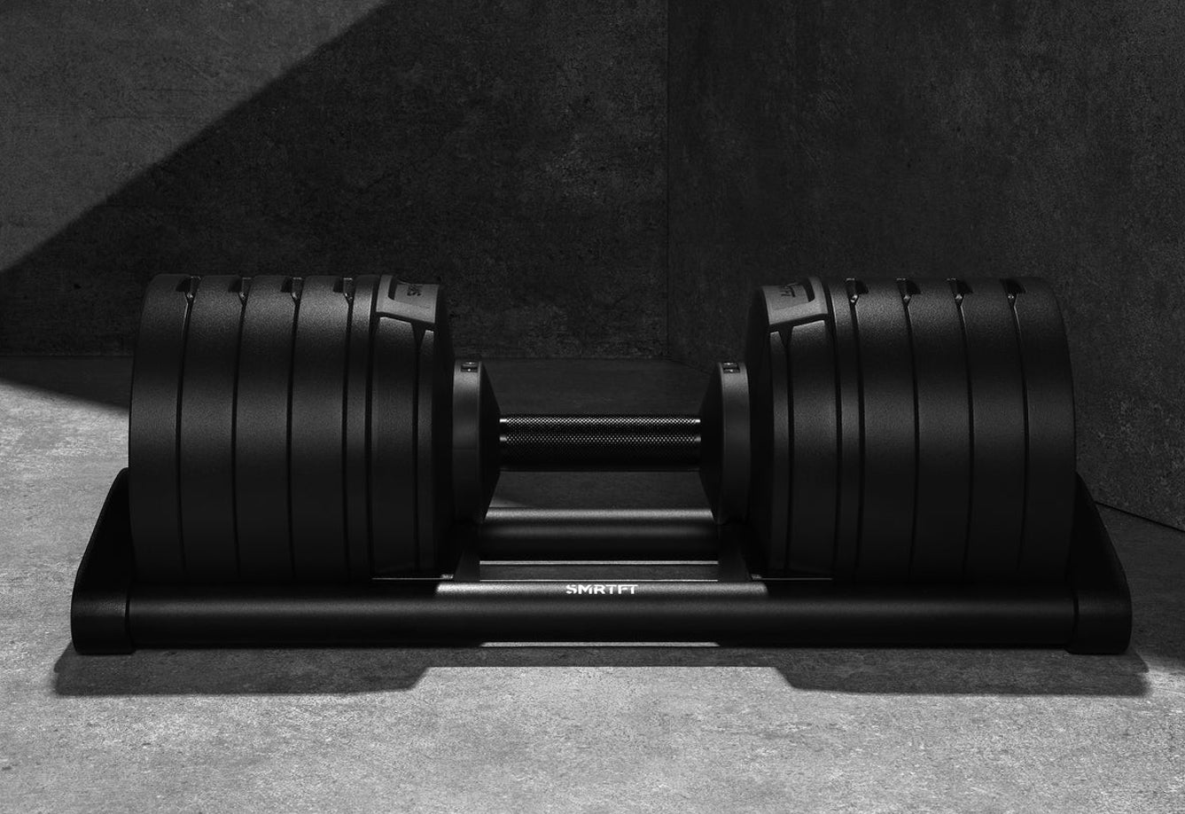Pair of black adjustable dumbbells with ribbed weight plates on matching base, viewed from above on concrete floor