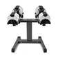 Pair of adjustable dumbbells with white and black striped heads mounted on black stand with central column, flat lay on white