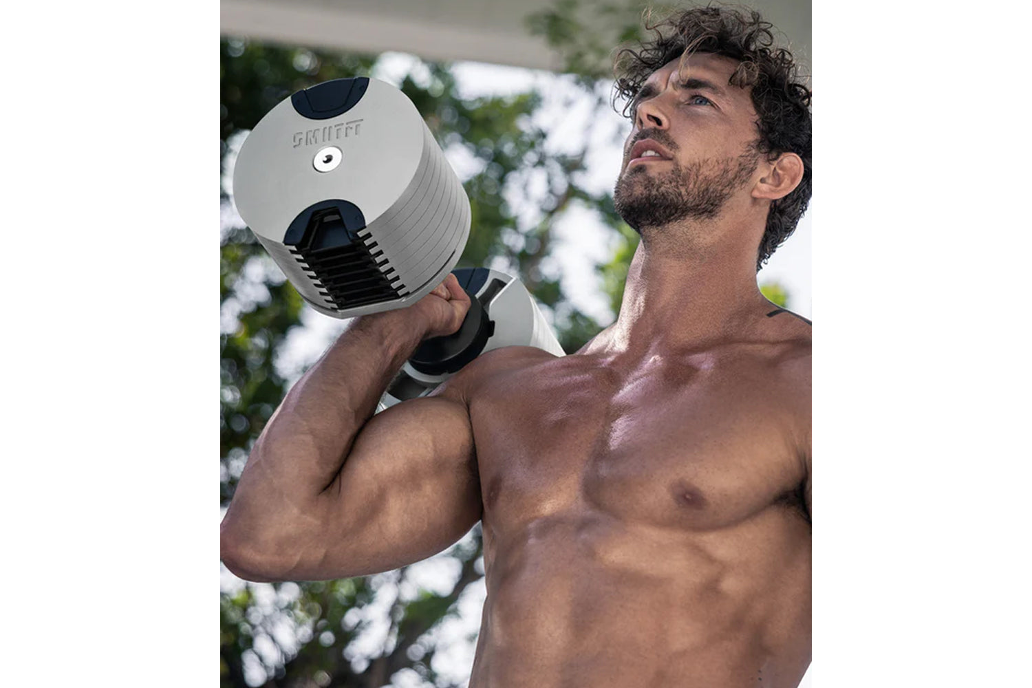 Man holding adjustable ash and black dumbbell outdoors, demonstrating weight training equipment