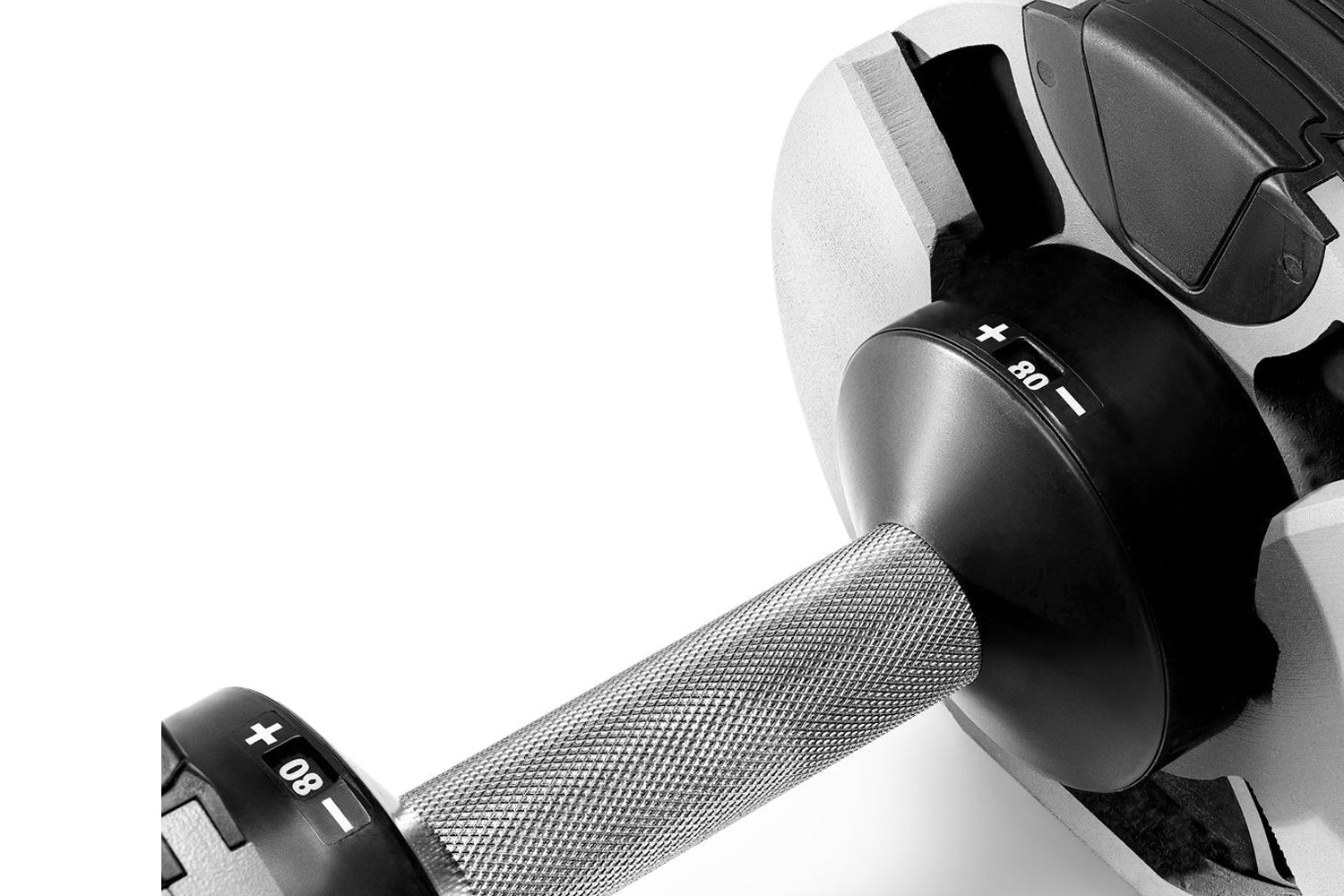 Pair of black and gray adjustable dumbbells with textured grip handles, weight markings visible on ends, flat lay on white ba