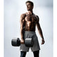 Muscular man wearing gray shorts holding matte black adjustable dumbbells, shown against white background