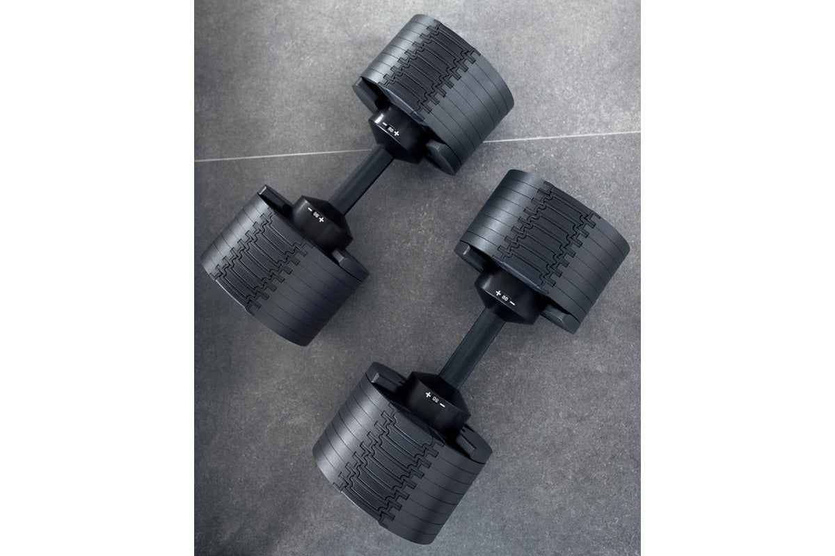 Three matte black adjustable dumbbells with ribbed weight plates and black handles on gray textured background