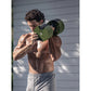 Man performing shoulder press with olive green adjustable dumbbell, shirtless, outdoors against gray wall