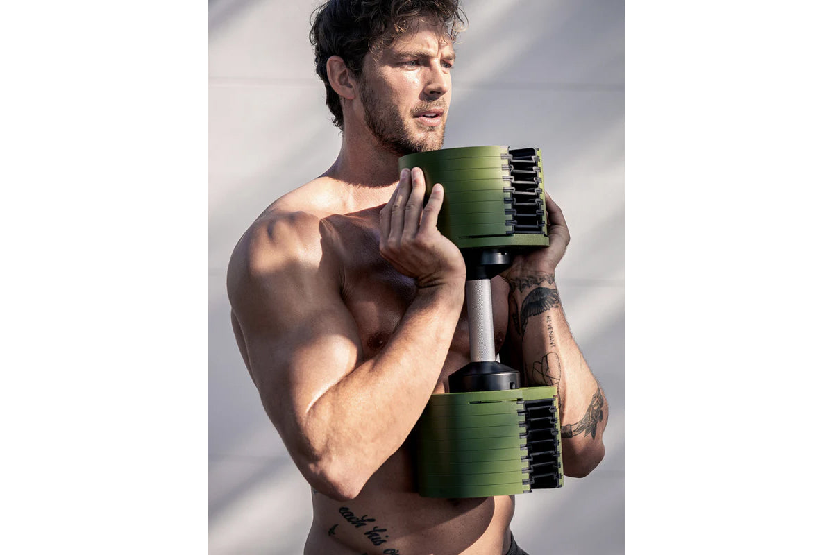 Man holding green and black adjustable dumbbells with weight increments, worn shirtless against white background
