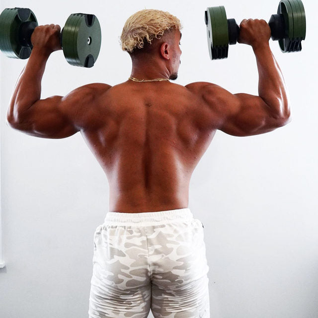 Shirtless man holding green and black adjustable dumbbells overhead, rear view, white background