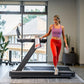 Woman running on black Octane OC220 treadmill in home gym, wearing purple sports bra and red leggings