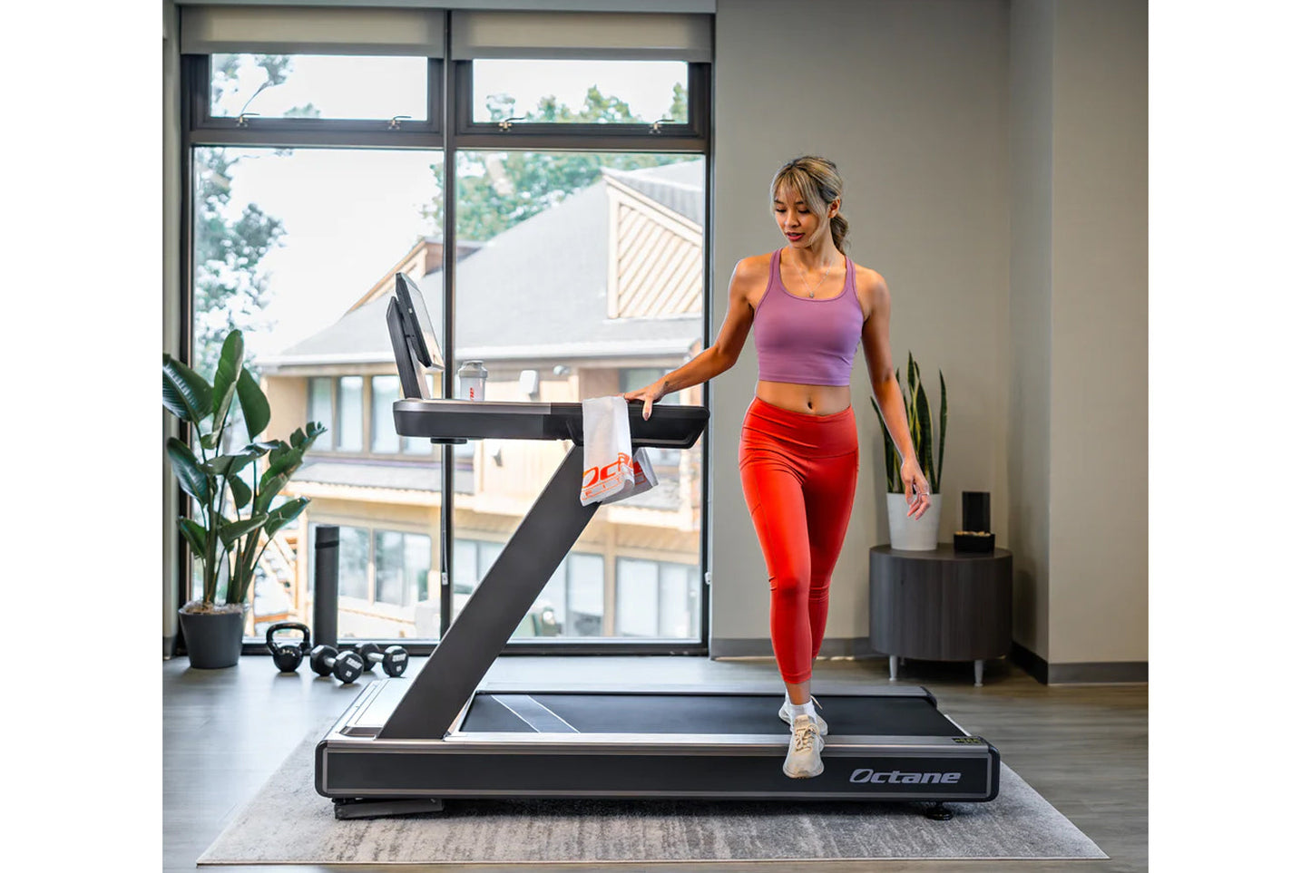 Woman running on black Octane OC220 treadmill in home gym, wearing purple sports bra and red leggings