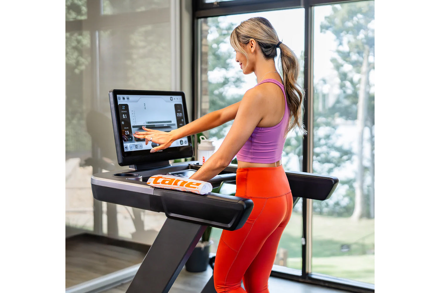Woman wearing purple sports bra and red leggings using Octane OC220 treadmill with touchscreen display in bright home gym