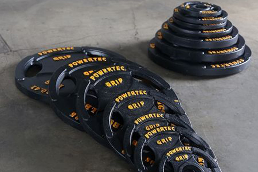 Powertec Olympic weight plates set in black rubber with yellow text markings, displayed in graduating sizes on concrete floor