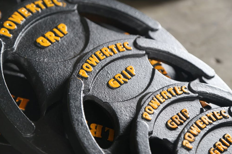 Gray Olympic weight plates with yellow "Powertec" and "Grip" text, stacked in flat lay arrangement