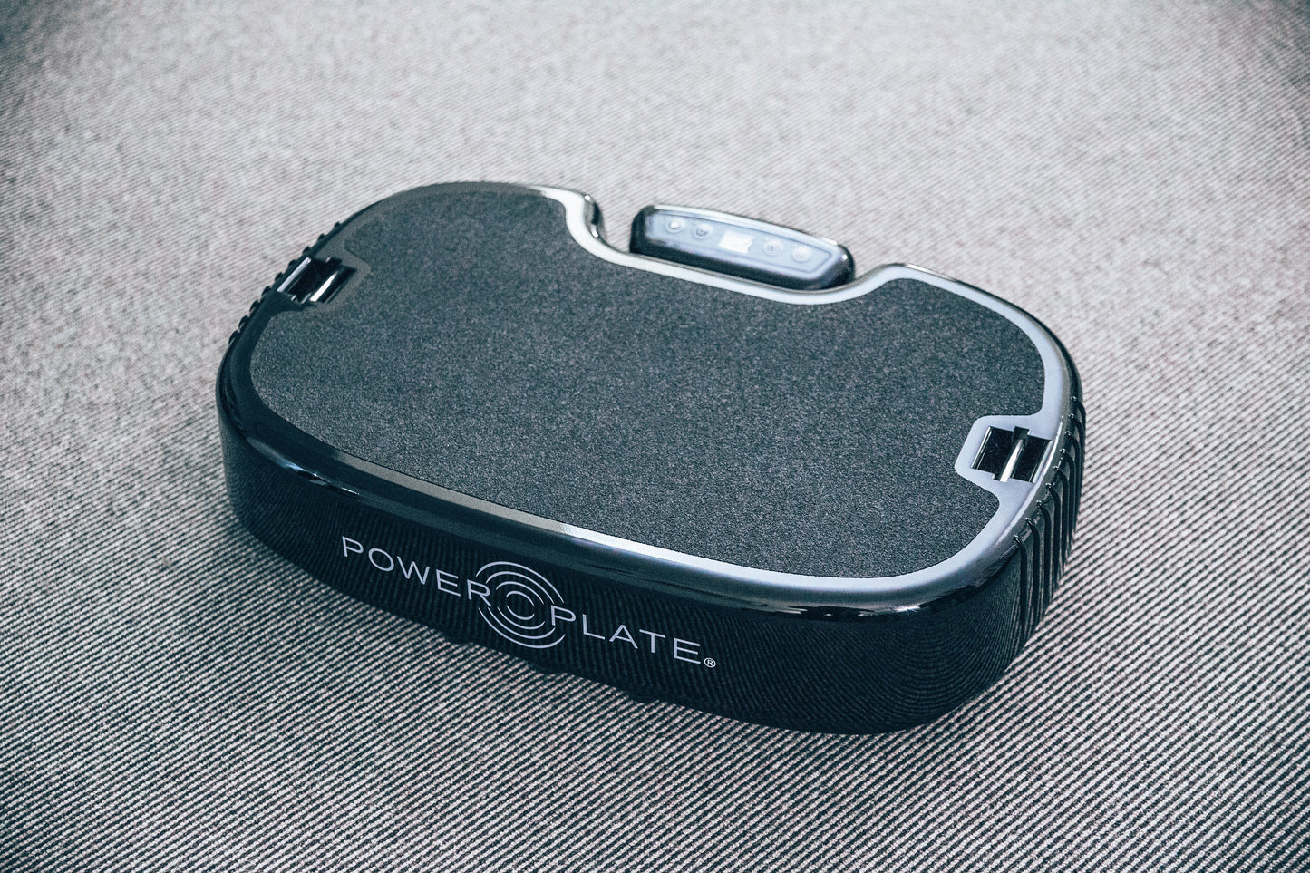 Power Plate Personal Vibration Machine — angled view showing textured non-slip surface, chrome trim, and control buttons on gray fabric background