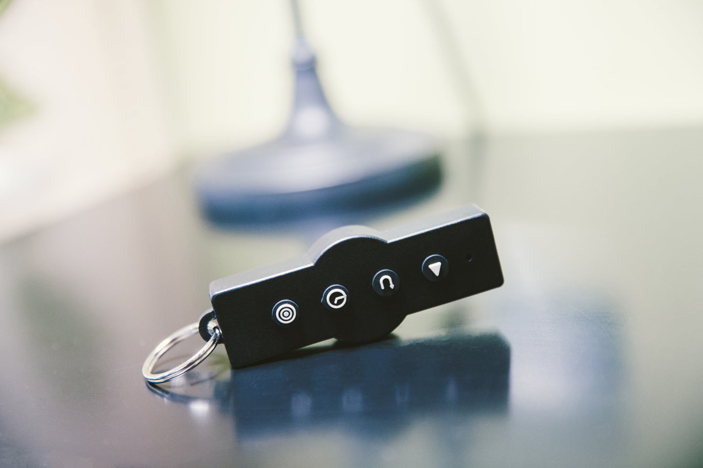 Black remote control with four illuminated buttons and metal key ring, displayed on blurred vibration machine background