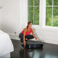 Woman in red tank top and black leggings using black Power Plate vibration machine in bedroom, worn by model