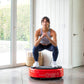 Woman in gray sports bra and navy leggings performing squat on red Power Plate MOVE vibration trainer in bright home gym with
