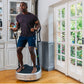 Man wearing charcoal t-shirt and navy shorts standing on white Power Plate My5 vibration trainer in home gym setting