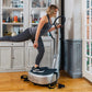Woman in gray tank top and striped black leggings using silver Power Plate My5 vibration trainer in home gym setting