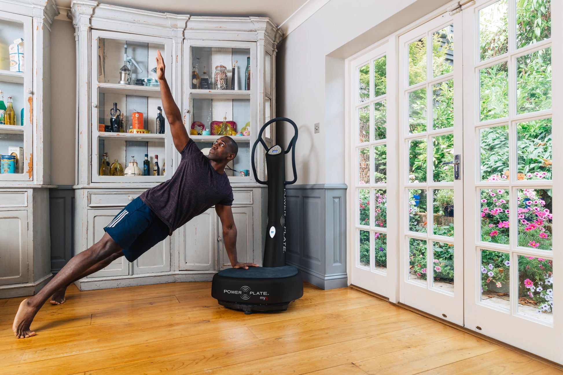 Man in plank position using black Power Plate My5 vibration trainer in bright home gym with white cabinetry and garden doors