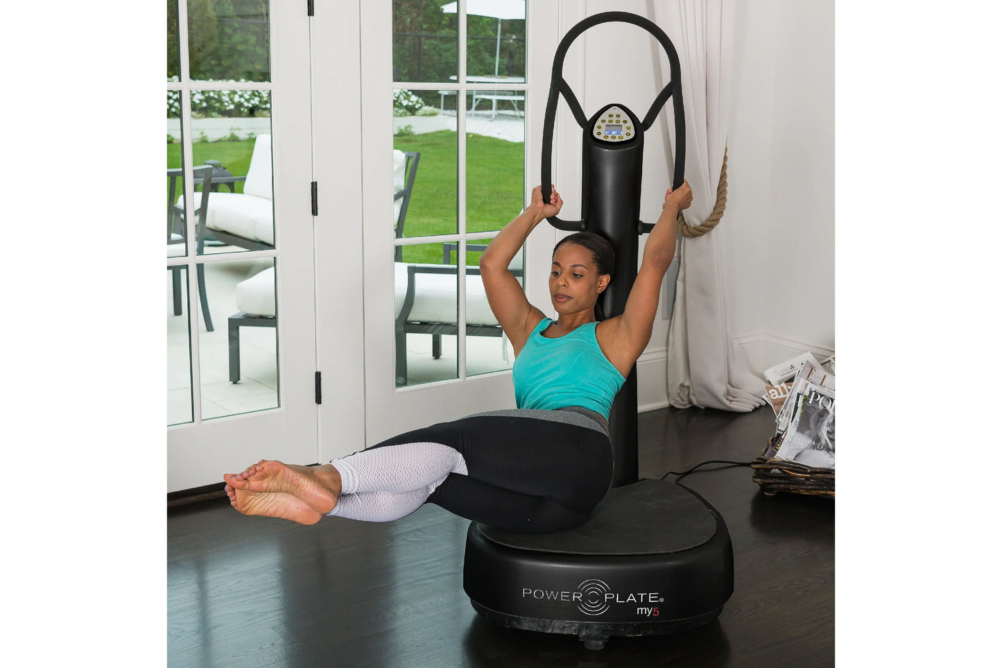 Woman in turquoise tank top and white leggings using black Power Plate My5 vibration trainer with resistance band in home gym