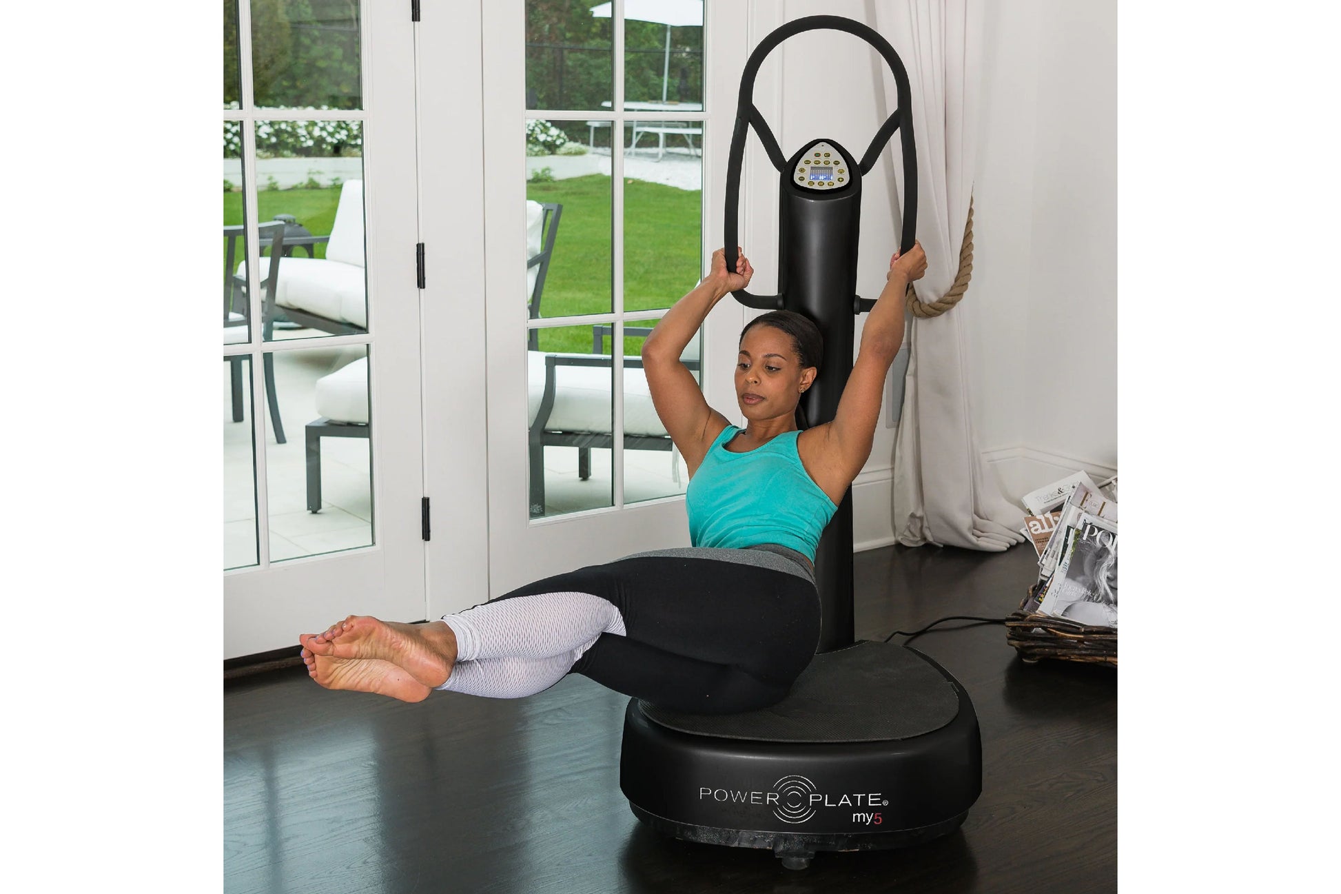 Woman in turquoise tank top and white leggings using black Power Plate My5 vibration trainer with resistance band in home gym