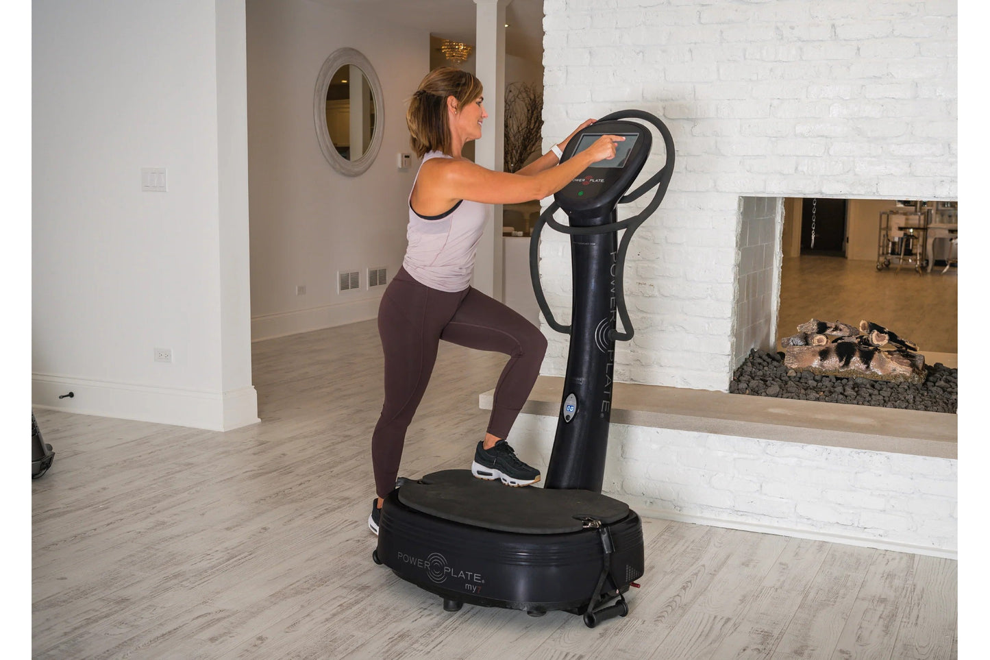 Woman wearing white tank top and burgundy leggings using black Power Plate My7 vibration trainer in fitness studio