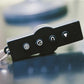 Black remote control with four silver icon buttons and metal keyring attached, on blurred background