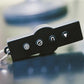 Black remote control with four white icon buttons and metal key ring on blurred background