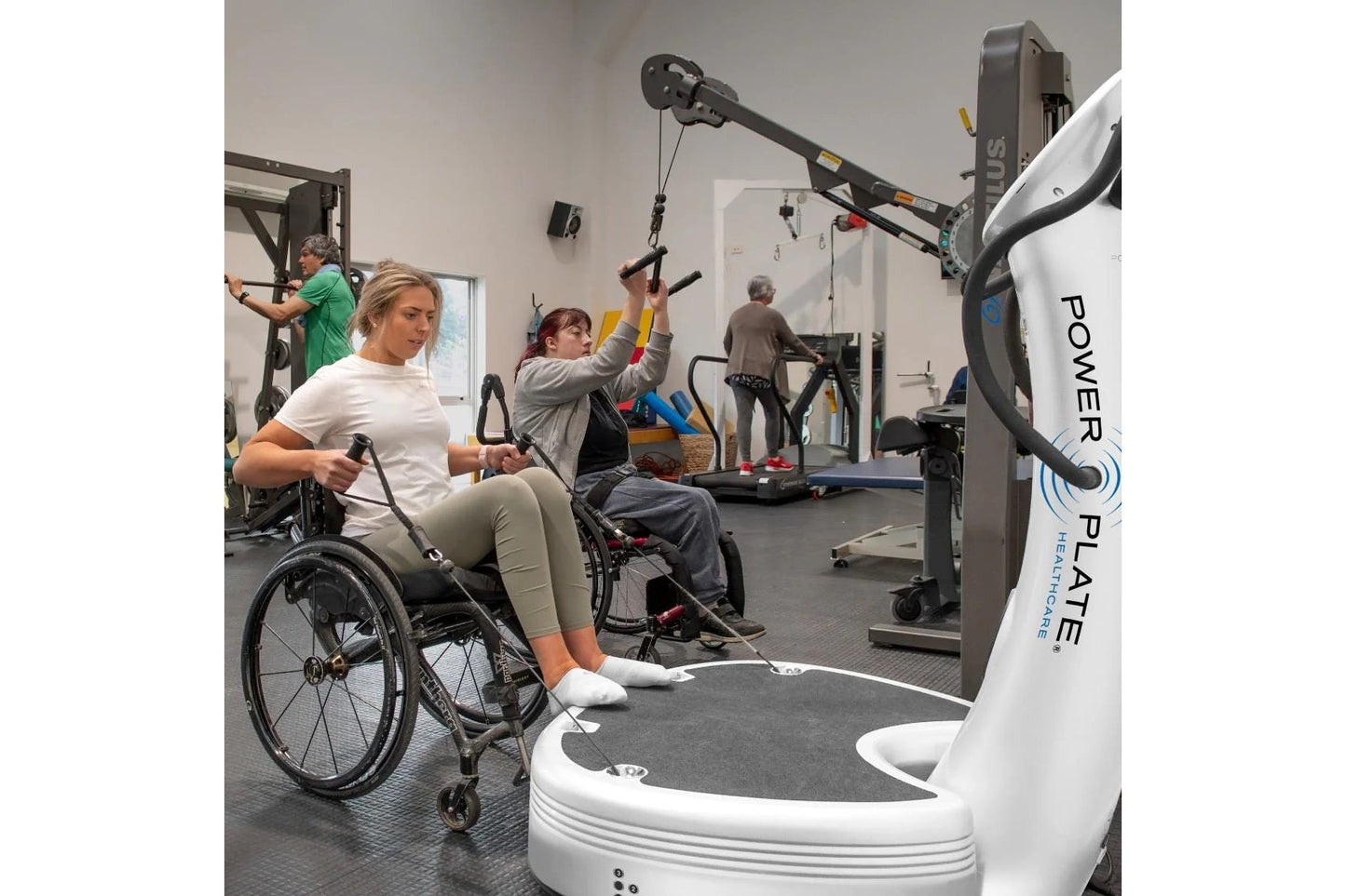 People using Power Plate vibration plate fitness equipment in accessible gym setting with wheelchair user in foreground